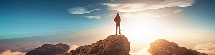 Kobieta stojąca tyłem na szczycie góry i patrząca w dal